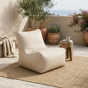 Sittsäck Fåtölj Seat 100 Outside Beige styled on a patio with a rug, wooden side table, and Mediterranean plants.